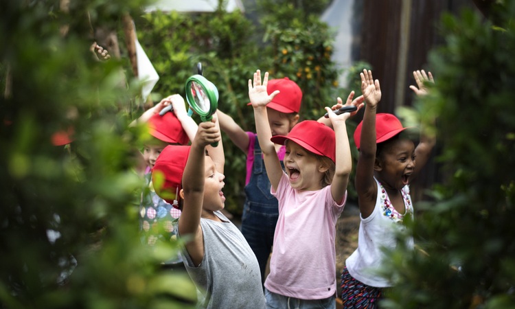 Kids smiling and raising their hands in the air on a field trip.